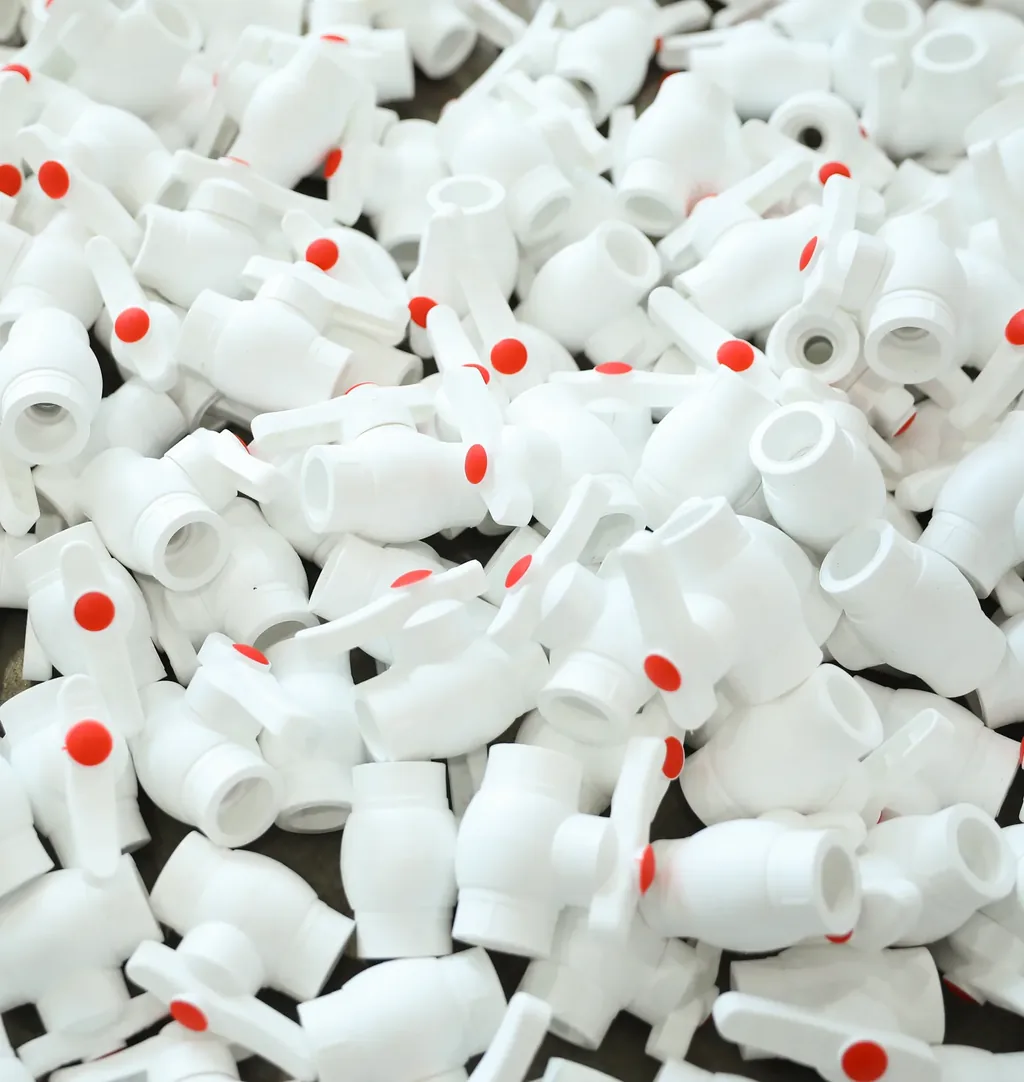 Bulk pile of white PPR ball valve bodies with red lever handles before assembly